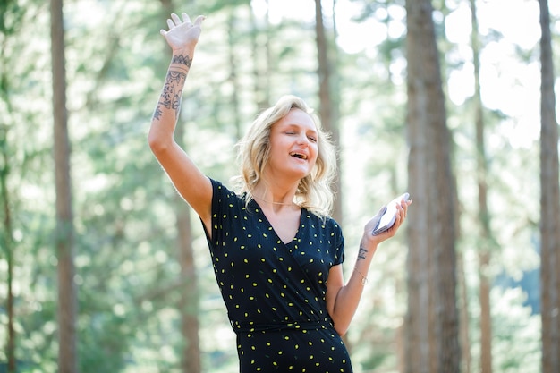 Une blogueuse heureuse danse en tenant un mobile sur fond de nature