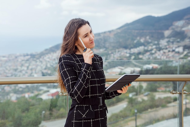 Une blogueuse pense en tenant un stylo planshet sur le temple sur fond de vue sur la ville