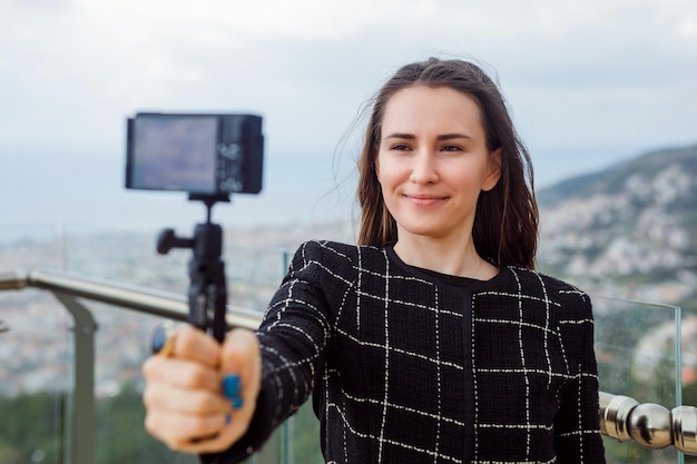 Une blogueuse prend un selfie en souriant à la caméra sur fond de vue sur la ville