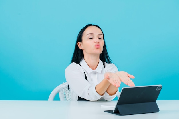 Une blogueuse souffle un baiser sur la caméra d'une tablette sur fond bleu