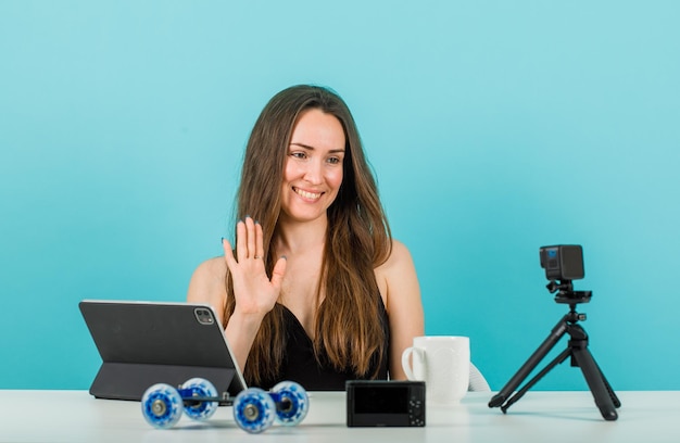 Une blogueuse souriante pose à la caméra en montrant un geste salut sur fond bleu