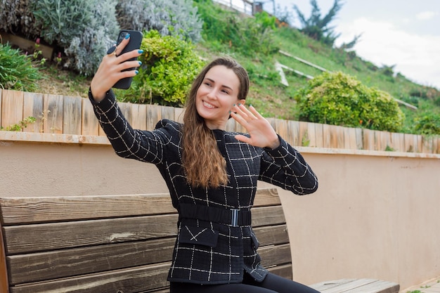 Une blogueuse souriante prend un selfie avec son smartphone en montrant son geste dans le parc