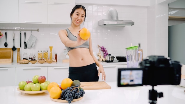 Blogueuse sportive asiatique utilisant une caméra enregistrant comment faire une vidéo de jus d'orange pour son abonné