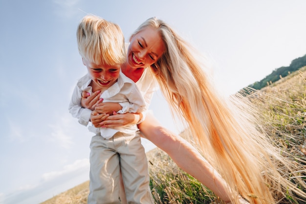 Blond petit garçon jouant avec maman aux cheveux blancs avec du foin dans le champ. été, temps ensoleillé, agriculture. enfance heureuse.