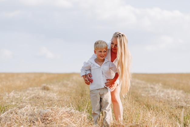 Blond petit garçon jouant avec maman aux cheveux blancs avec du foin dans le champ. été, temps ensoleillé, agriculture. enfance heureuse.