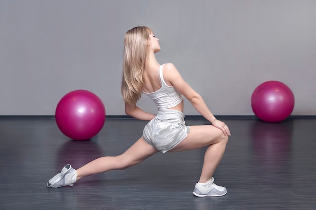 Blond Sporty Caucasian Lady est dans la salle de gym pendant l'entraînement, des exercices pour étirer les muscles des jambes. Échauffement avant l'entraînement. Remise en forme des femmes.