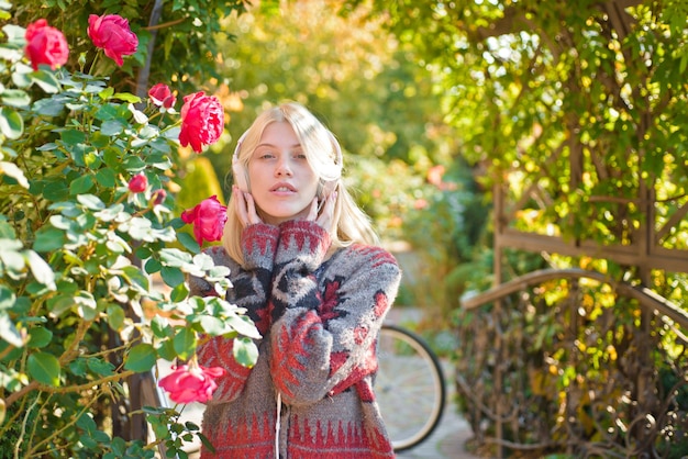 Blonde apprécie la musique dans un parc ou un jardin. Fille active avec des écouteurs. Musique favorite. Casque femme jardin fleuri. Activité du week-end. Loisirs actifs et style de vie. Fille écouter de la musique et faire du vélo.