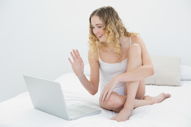 Blonde assez souriante assise sur le lit en agitant au portable