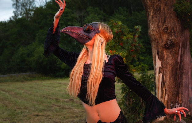 Blonde au masque de corbeau pose dans la nature près du vieil arbre