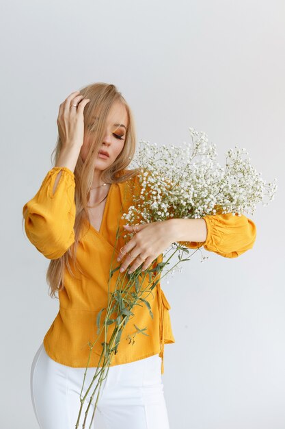 Blonde aux cheveux longs en bonne santé avec des fleurs délicates et du maquillage sur fond gris. affiche. beauté