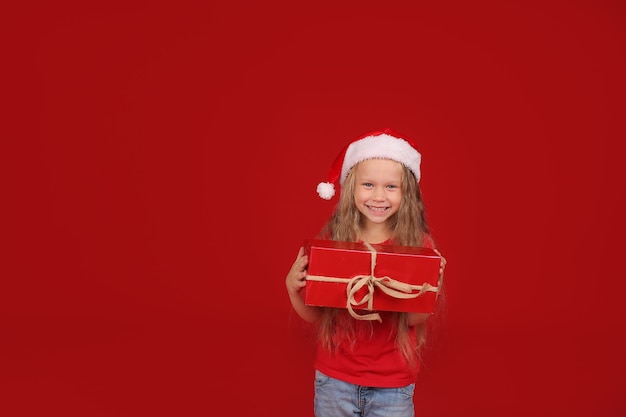 blonde aux yeux bleus dans un Tshirt rouge dans un chapeau de père Noël tenant une boîte-cadeau