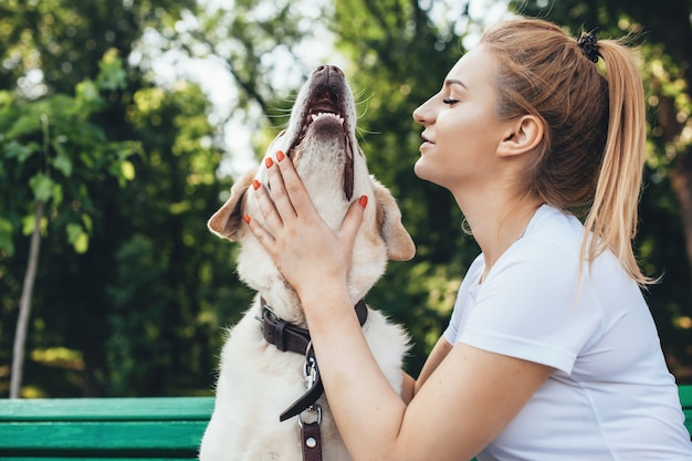 Blonde caucasienne femme joue avec son chien assis sur un banc lors d'une promenade dans le parc.