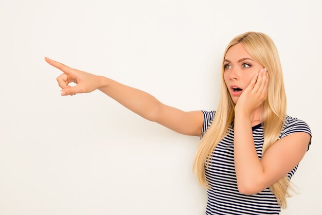 Blonde choquée touchant son visage et pointant du doigt