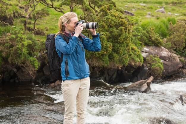 Blonde debout sur le rocher dans un ruisseau en prenant une photo