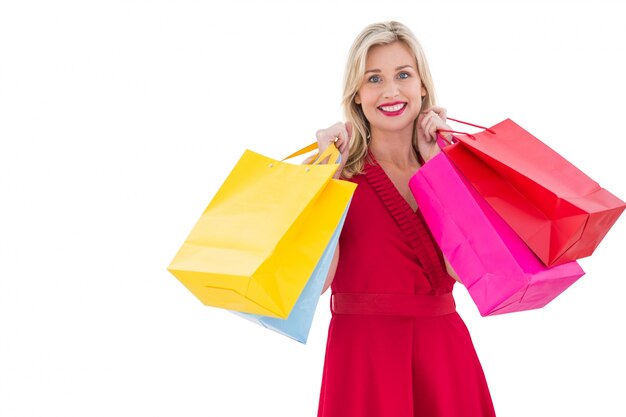 Blonde élégante en robe rouge tenant des sacs à provisions