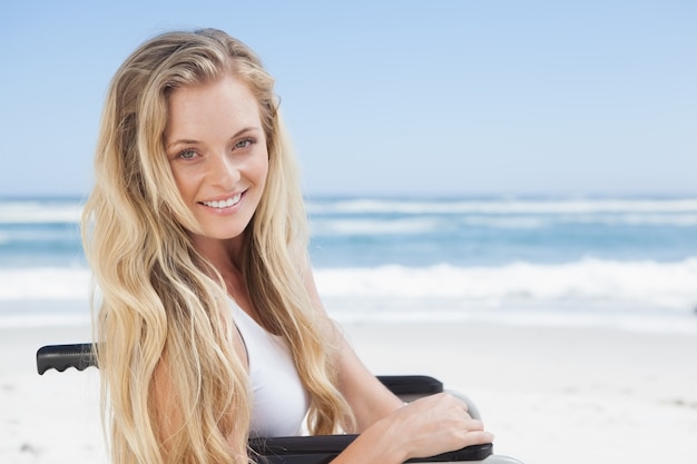 Blonde en fauteuil roulant, souriant à la caméra sur la plage