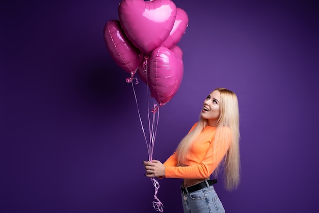 Blonde heureuse avec des ballons en forme de coeur sur violet