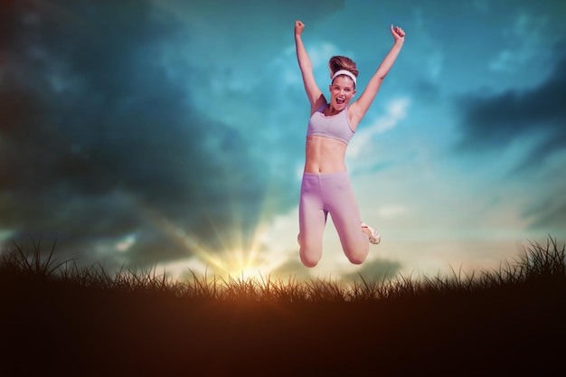 Blonde heureuse sportive sautant contre le ciel bleu au-dessus de l'herbe