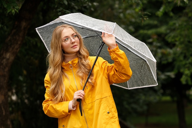 Blonde en imperméable jaune avec parapluie sous la pluie sur fond vert