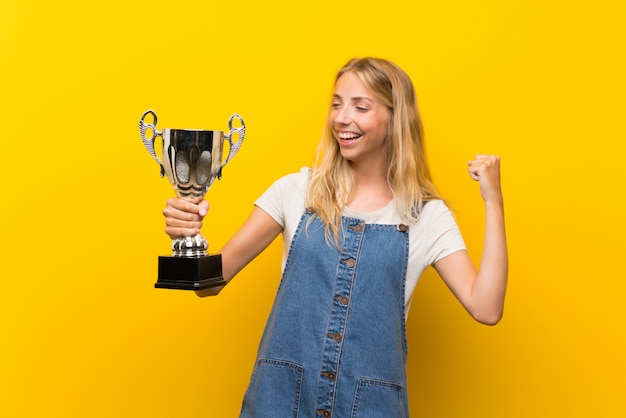 Blonde Jeune Femme Sur Un Mur Jaune Isolé Tenant Un Trophée