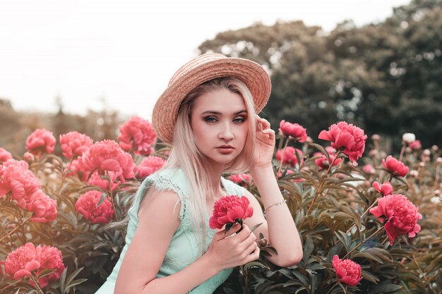 Blonde jeune femme en pivoines en fleurs roses, fille regarde dans le cadre