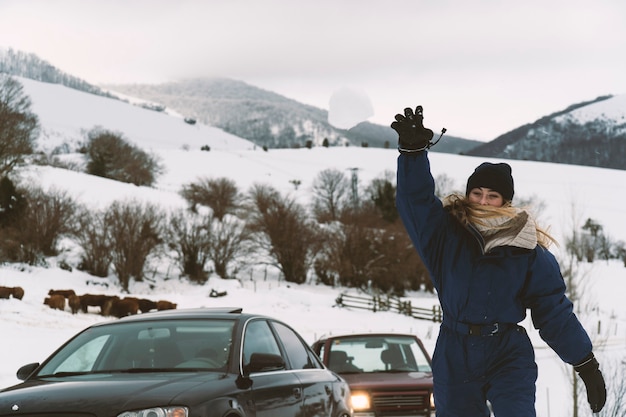 Photo blonde jeune fille lançant une boule de neige à la caméra dans les montagnes
