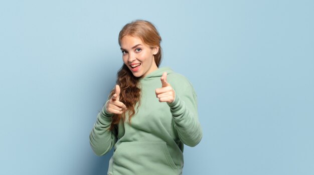 Blonde jolie femme souriante avec une attitude positive, réussie, heureuse de pointage, faisant signe de pistolet avec les mains