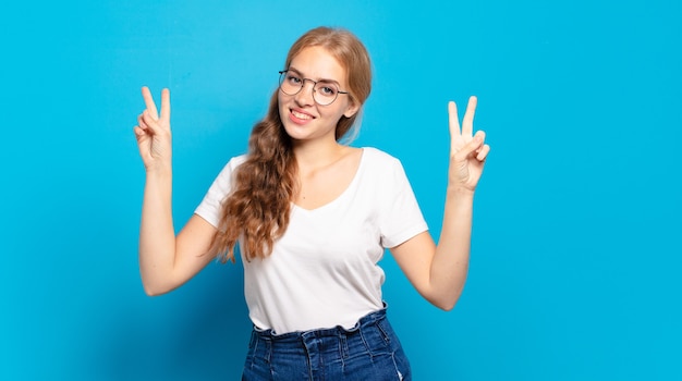 Blonde jolie femme souriante et à la recherche heureuse, sympathique et satisfaite, gesticulant la victoire ou la paix à deux mains