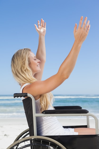 Blonde ligotée en fauteuil roulant, souriant sur la plage