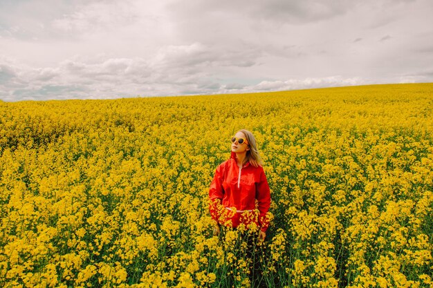 Blonde en lunettes de soleil et survêtement rouge dans le champ de colza