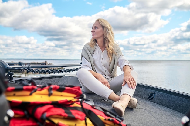 Une blonde mature woman in white clothes assis sur un bateau et à la rêveuse