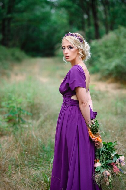 Blonde modèle fille dans une robe lilas avec un bouquet avec une forêt verte