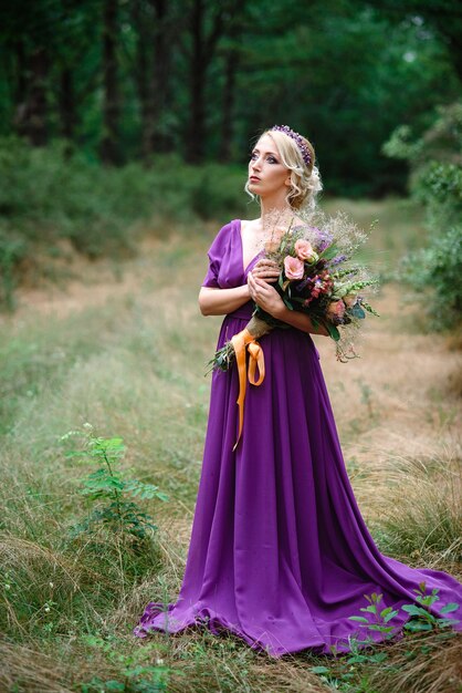 Blonde modèle fille dans une robe lilas avec un bouquet avec une forêt verte