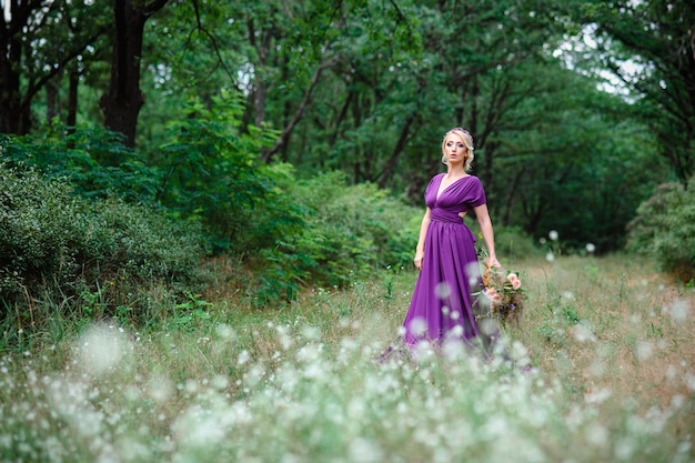 Blonde modèle fille dans une robe lilas avec un bouquet avec une forêt verte