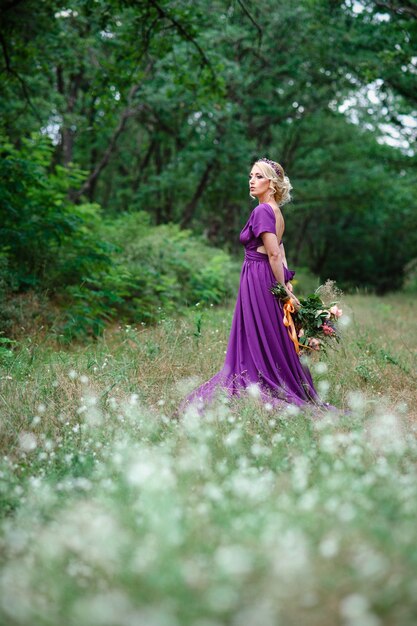 Blonde modèle fille dans une robe lilas avec un bouquet avec une forêt verte