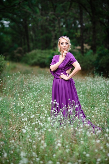 Blonde modèle fille dans une robe lilas avec un bouquet avec une forêt verte