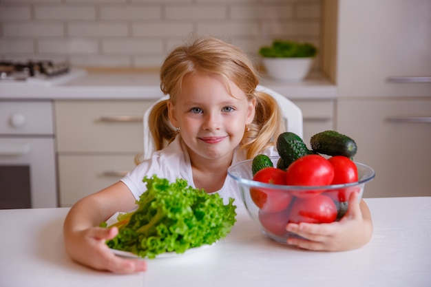 Blonde petite fille mangeant des légumes dans la cuisine