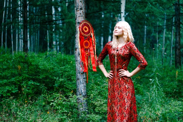 Blonde en robe rouge dans les bois à côté d'un capteur de rêves