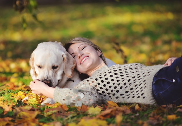 La blonde se trouve dans les feuilles jaunes avec son labrador dans le parc en automne