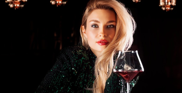 Blonde séduisante dans une robe de soirée verte posant avec un verre de vin rouge. Technique mixte