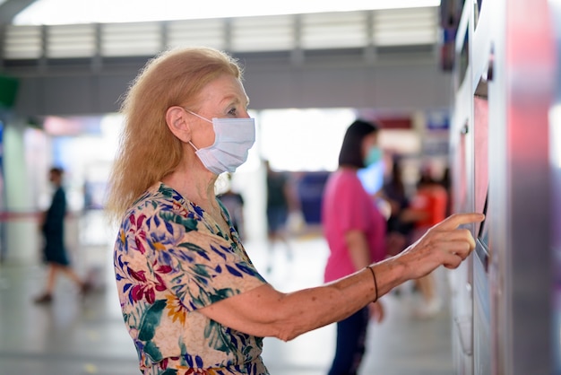 Blonde Senior Woman Avec Masque D'achat De Billets à La Gare Du Ciel