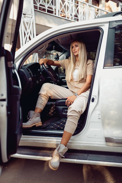 Blonde sensuelle dans des vêtements élégants posant dans une belle voiture. Voitures et filles