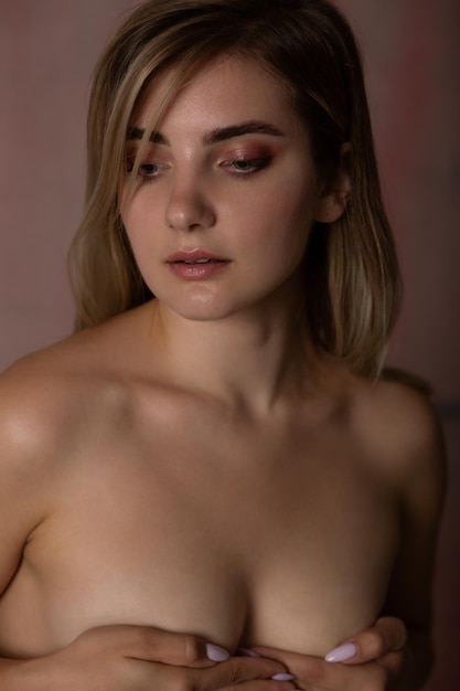 Photo blonde sexy avec du maquillage couvre ses seins avec ses mains