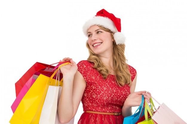 Blonde souriante au bonnet de Noel tenant des sacs à provisions