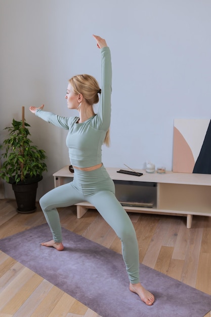 Blonde en survêtement pratiquant le yoga à la maison