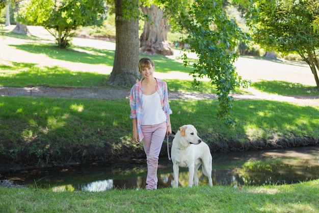 Blonde très souriante, marchant avec son labrador dans le parc