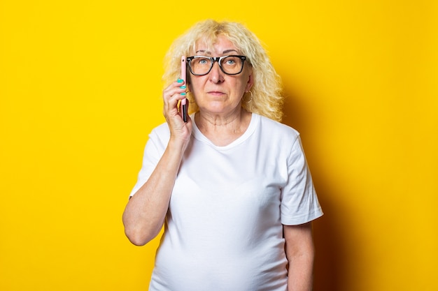 Blonde vieille femme bouclée dans un T-shirt blanc, avec des lunettes de parler au téléphone