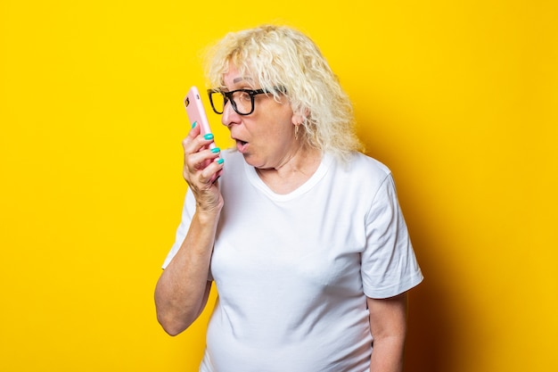 Blonde vieille femme bouclée en t-shirt blanc crie tout en parlant au téléphone