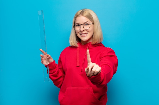 Blonde woman smiling fièrement et en toute confiance faisant le numéro un pose triomphalement, se sentant comme un leader