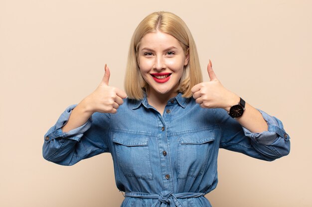 Blonde woman smiling globalement à la recherche heureuse, positive, confiante et réussie, avec les deux pouces vers le haut